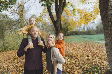 Parents giving piggyback ride to children in autumn forest - AANF00425