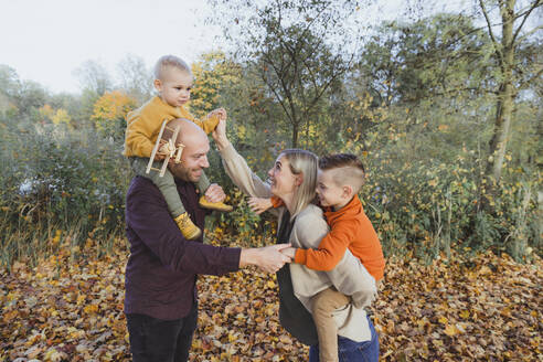 Glückliche Eltern mit Kindern, die sich im Herbstwald vergnügen - AANF00426