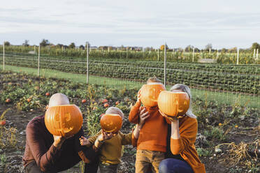 Eltern mit Kindern bedecken ihre Gesichter mit Lampions auf einem Feld - AANF00456