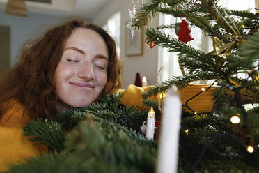 Smiling woman with eyes closed hugging Christmas tree at home - TYF00640