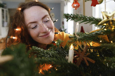 Smiling woman with string lights on head embracing Christmas tree - TYF00641