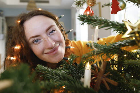 Lächelnde Frau mit Weihnachtsbeleuchtung auf dem Kopf zu Hause - TYF00642