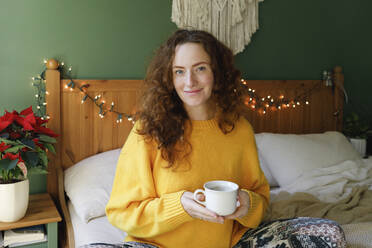 Lächelnde Frau mit einer Tasse Tee auf dem Bett zu Hause - TYF00652