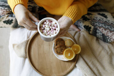 Frau hält Becher mit heißer Schokolade mit Marshmallows auf dem Bett - TYF00654