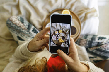 Frau fotografiert Essen mit dem Smartphone auf dem Bett zu Hause - TYF00657