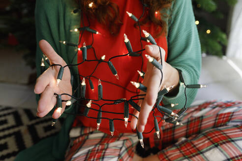 Hands of woman with illuminated tangled string lights at home - TYF00674