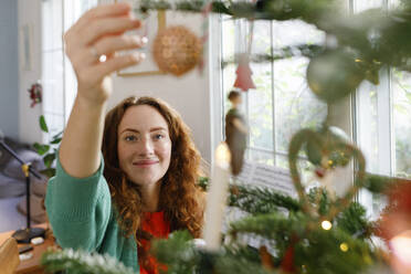 Lächelnde Frau beim Schmücken des Weihnachtsbaums zu Hause - TYF00677