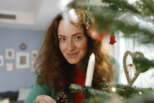 Lächelnde Frau betrachtet den Weihnachtsbaum zu Hause - TYF00678