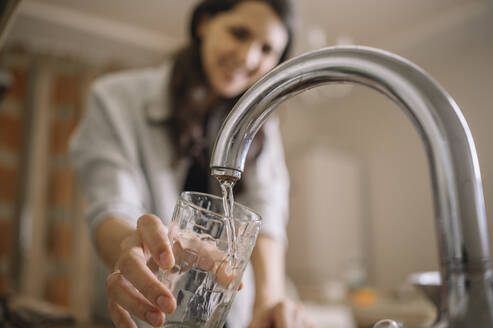 Frau füllt Wasser aus dem Wasserhahn in ein Glas zu Hause - ANAF00821