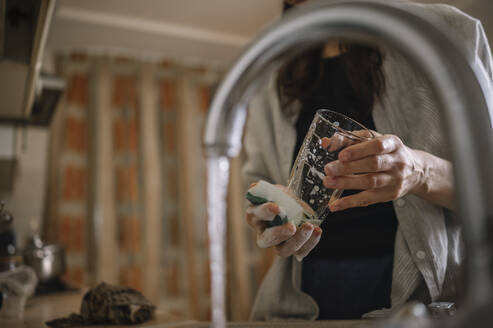 Frau wäscht Trinkglas vor fließendem Wasser aus dem Wasserhahn zu Hause - ANAF00822