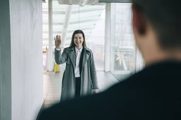 Glückliche Geschäftsfrau winkt einem Kollegen auf dem Bahnhof zu - AMWF01089