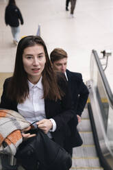 Businesswoman moving up on escalator with colleague at station - AMWF01097
