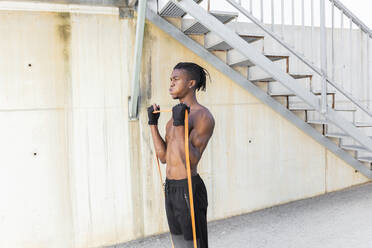 Shirtless man exercising with resistance band outdoors - JPTF01250