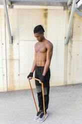 Shirtless young man exercising with resistance band outdoors - JPTF01251