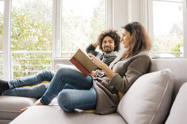 Man with woman reading book on sofa at home - MOEF04439