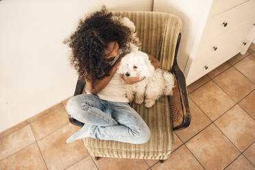 Mädchen sitzt mit Hund auf einem Stuhl zu Hause - MOEF04444