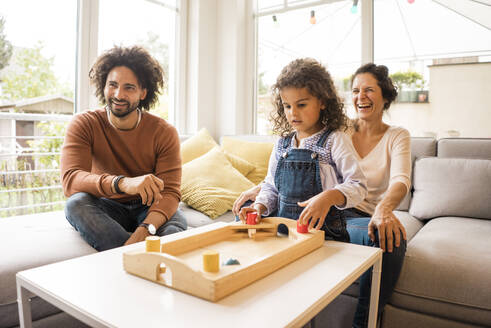 Glücklicher Mann und Frau mit Tochter spielen Brettspiel im Wohnzimmer zu Hause - MOEF04445