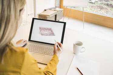 Junge Frau zeichnet Solarpanel auf Laptop am Schreibtisch - UUF27939