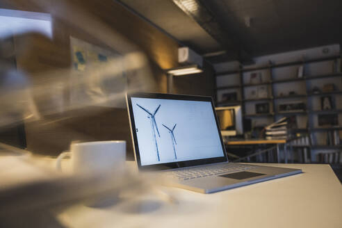 Laptop with drawing of wind turbine at desk - UUF27963