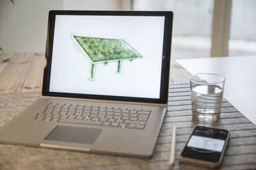 Zeichnung eines Solarpanels auf einem Laptop-Bildschirm, der von einem Smartphone am Schreibtisch gehalten wird - UUF27969