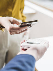 Hand of young businesswoman paying through smart phone on credit card reader - UUF27974