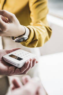 Hand of young businesswoman paying with smart watch on credit card reader - UUF27977