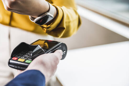 Hand of young businesswoman paying with smart watch on card reader machine - UUF27978