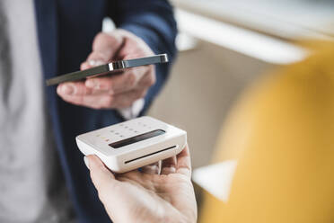 Hand of businessman paying with smart phone on card reader machine - UUF27986