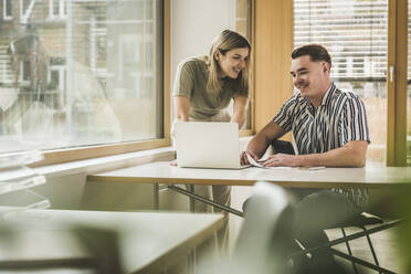 Smiling businesswoman and businessman discussing over laptop in office - UUF27996