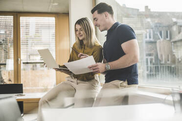 Young businessman and businesswoman discussing over laptop in office - UUF28003