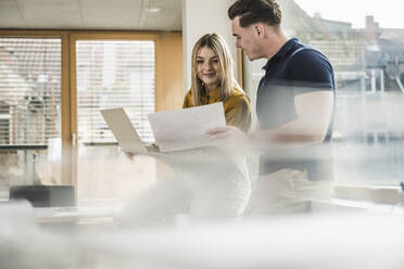 Smiling young businesswoman discussing over document with colleague in office - UUF28005