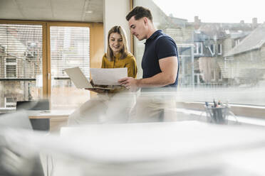 Happy young businesswoman discussing over document with colleague in office - UUF28006