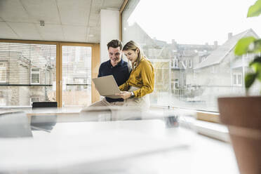 Young businessman with businesswoman working on laptop in office - UUF28008