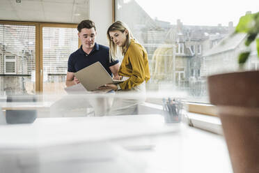 Businessman with colleague working on laptop in office - UUF28009