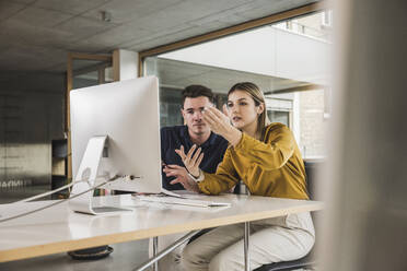 Junge Geschäftsfrau gestikuliert und diskutiert über Desktop-PC im Büro - UUF28018