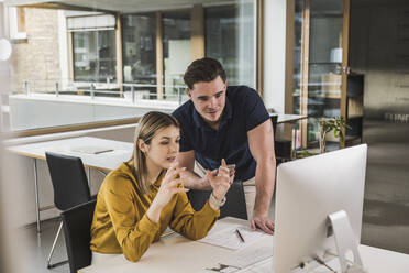 Businesswoman gesturing and having discussion over desktop PC in office - UUF28020