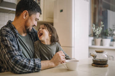 Happy father having fun with son sitting in kitchen at home - ANAF00830