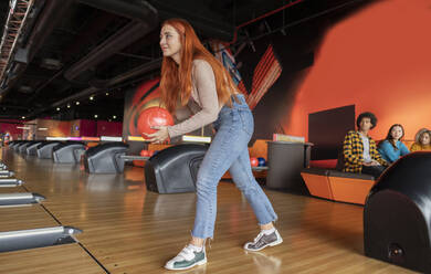 Junge Frau wirft Ball mit Freunden sitzen im Hintergrund auf der Bowlingbahn - JCCMF08774