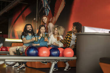 Gemischtrassige Freunde trinken Bier auf dem Sofa in einer Bowlingbahn - JCCMF08796