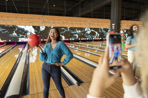 Frau fotografiert Freund mit Smartphone in Bowlingbahn - JCCMF08807