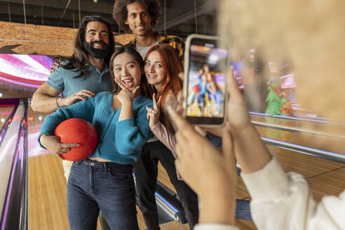 Junge Frau fotografiert ihre Freunde mit dem Handy auf einer Bowlingbahn - JCCMF08810