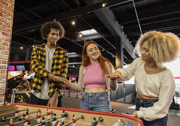 Happy woman holding hands with friends standing in arcade - JCCMF08819