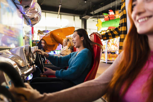 Junge Frauen haben Spaß mit einem Fahrsimulator in einer Spielhalle - JCCMF08824