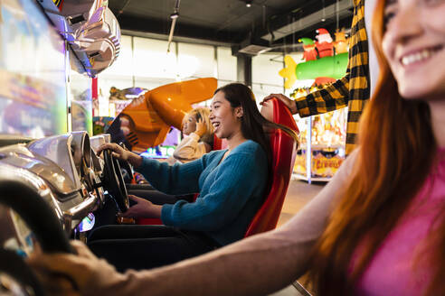 Young women having fun with driving simulator in arcade - JCCMF08824