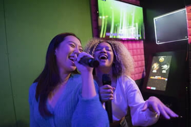 Glückliche junge Freunde singen Karaoke mit Mikrofon in einer Spielhalle - JCCMF08845