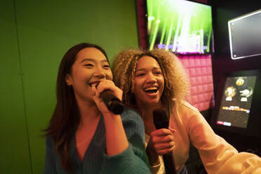 Glückliche Frauen haben Spaß beim Karaoke-Singen in einer Spielhalle - JCCMF08846