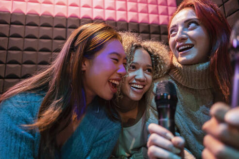 Glückliche junge Frauen singen Karaoke mit Mikrofon in einer Spielhalle - JCCMF08849