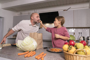 Daughter feeding father in kitchen at home - KMKF01908