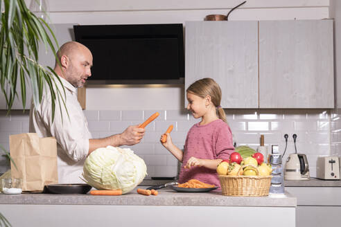 Vater und Tochter haben Spaß mit Karotten in der Küche zu Hause - KMKF01912