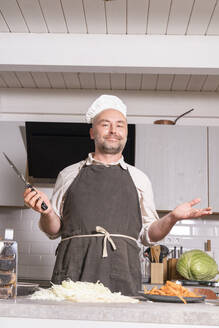 Portrait of man wearing chef clothing in kitchen at home - KMKF01920